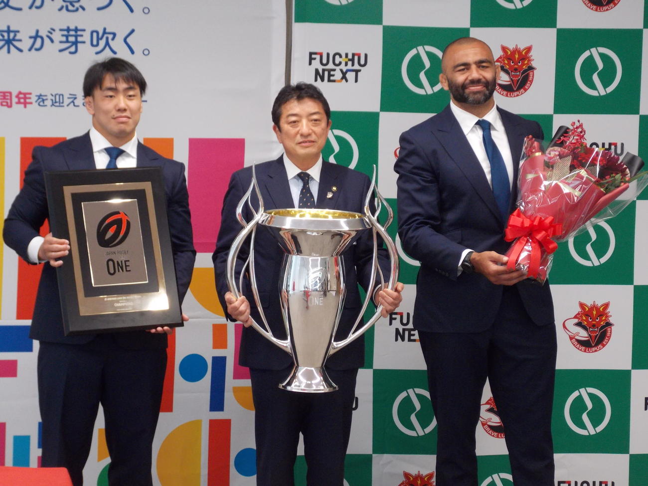 府中市役所を表敬訪問し、手渡された優勝トロフィーを持つ高野律雄市長（中央）とBL東京リーチ・マイケル（右）、原田衛（左）（撮影・松本航）