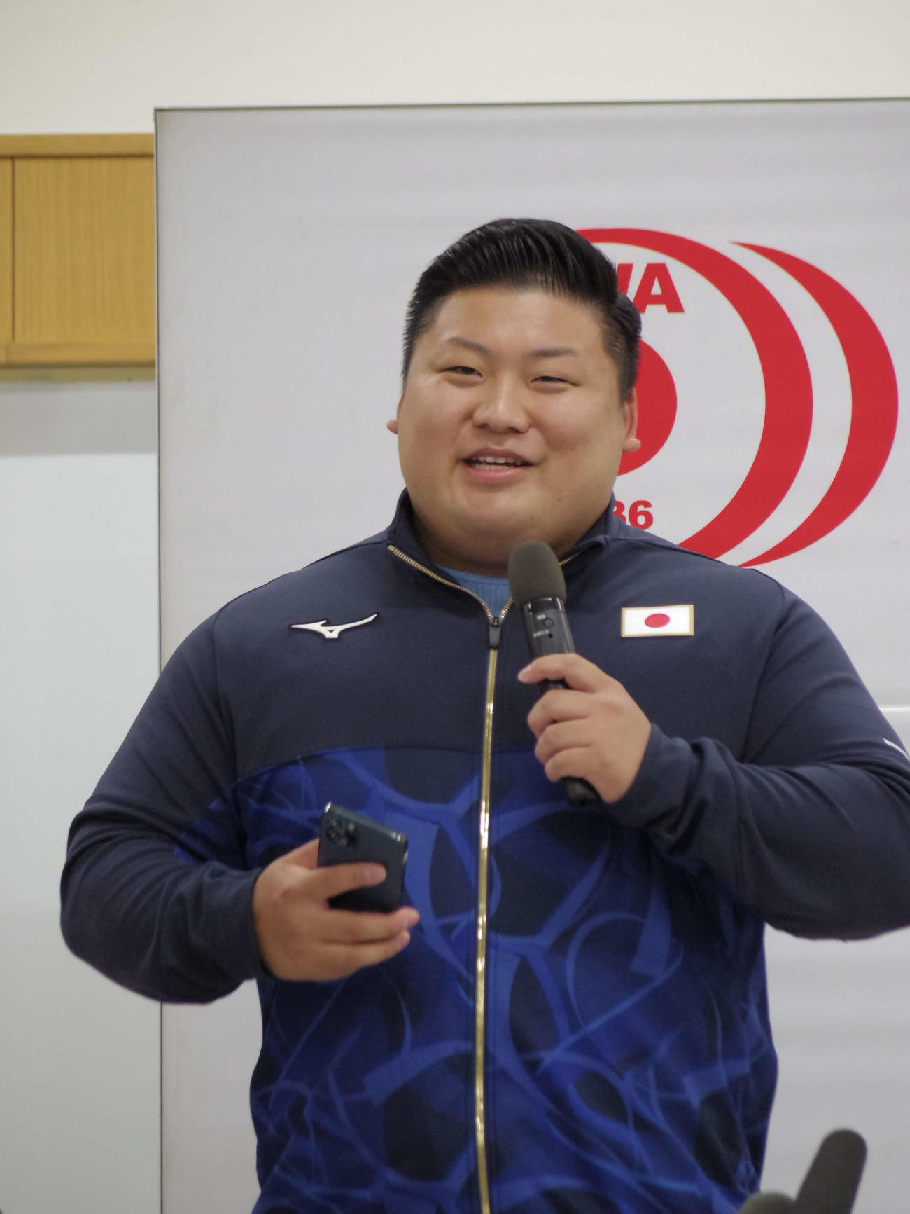 パリ五輪日本代表に内定し、スピーチ内容をメモをしたスマホを片手に喜びと意気込みを語る重量挙げ男子102キロ長久の村上英士朗