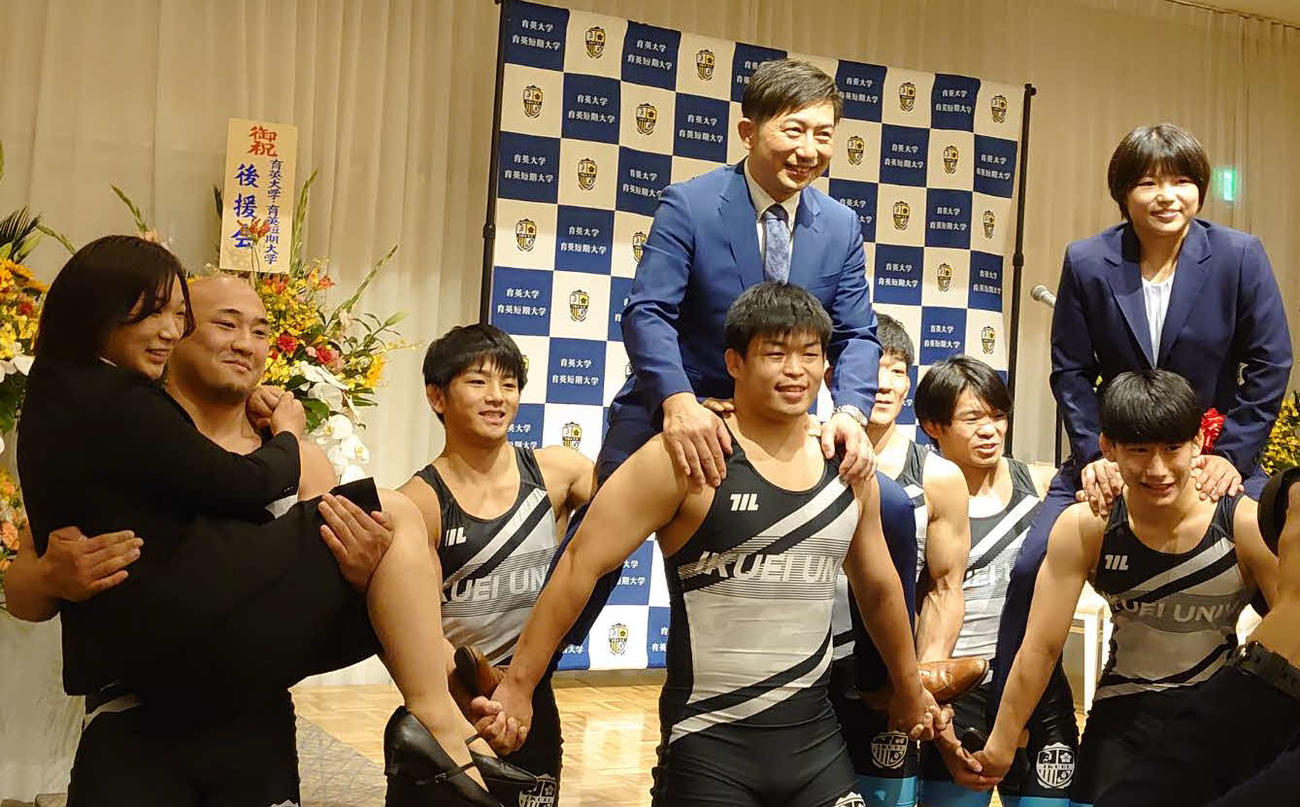 育英大レスリング部員にお姫様だっこをされる元木咲良（左）と、担がれる桜井つぐみ（右）と柳川美麿監督（撮影・飯岡大暉）