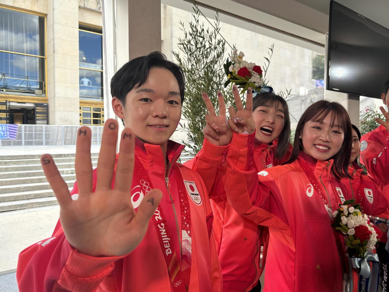 北京五輪団体のメダル授与式で、欠席となった宇野昌磨さんの名前を指に記した左から鍵山優真、坂本花織、樋口新葉
