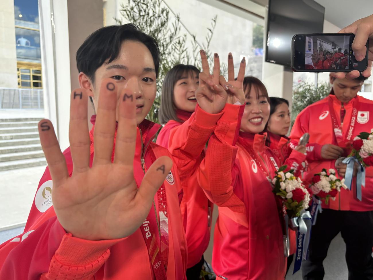 北京五輪団体のメダル授与式で、欠席となった宇野昌磨さんの名前を指に記した左から鍵山優真、坂本花織、樋口新葉