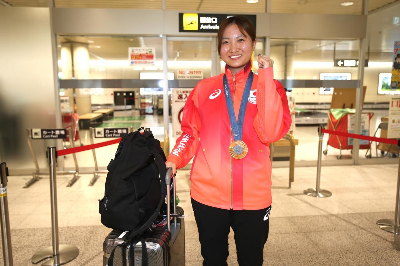 尾崎は銅メダルを首からかけて笑顔で新千歳空港でガッツポーズ（撮影・中島洋尚）
