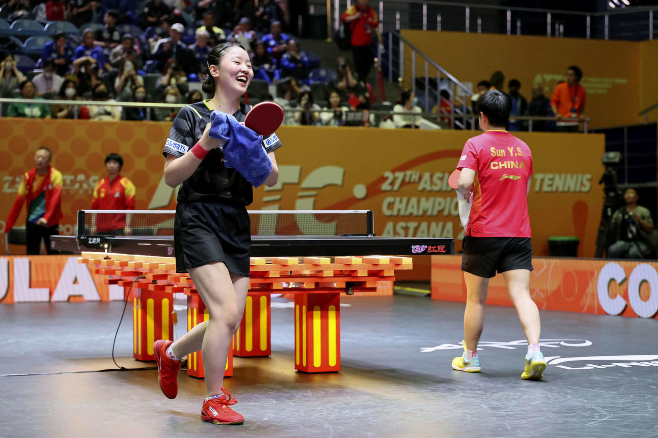 女子団体決勝で中国の孫穎莎（右）と対戦し、笑顔を見せる張本美和（共同）