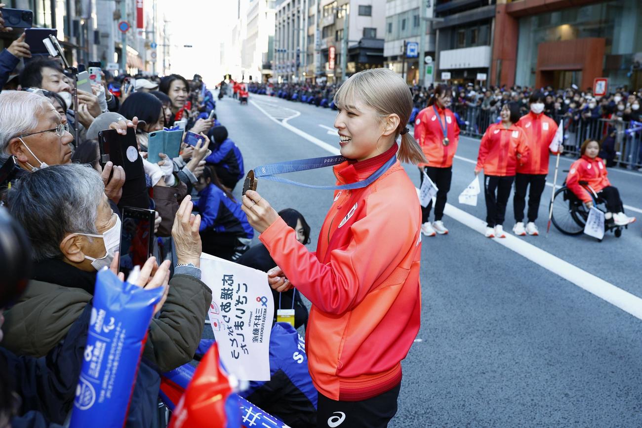パリ五輪・パラリンピックの日本選手団による応援感謝イベントで、沿道に集まった人にメダルを見せるフェンシング女子の江村美咲（共同）