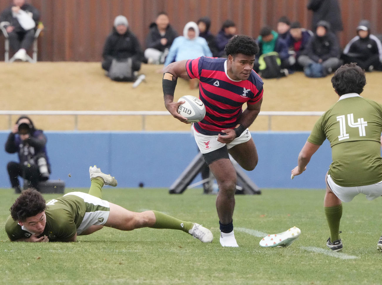 大東大対京産大　前半、相手タックルを受け右スパイクが脱げるも突進する京産大ナブラギ・エロニ（中央）（撮影・森本幸一）
