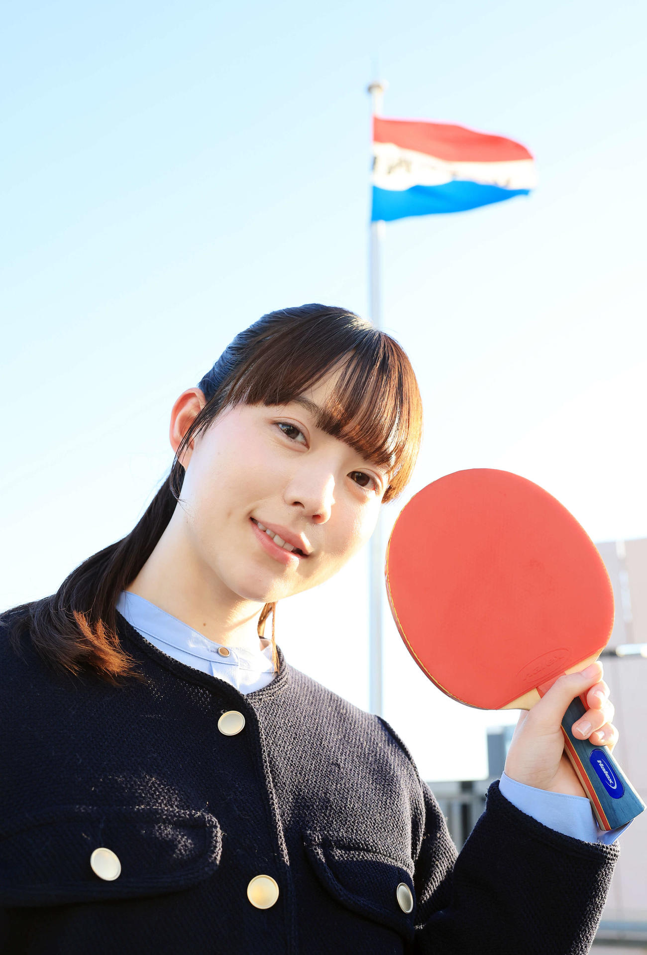 2025年2月25日、来社した“卓球天使”の菊池日菜は日刊スポーツの社旗を背にほほ笑む（撮影・浅見桂子）