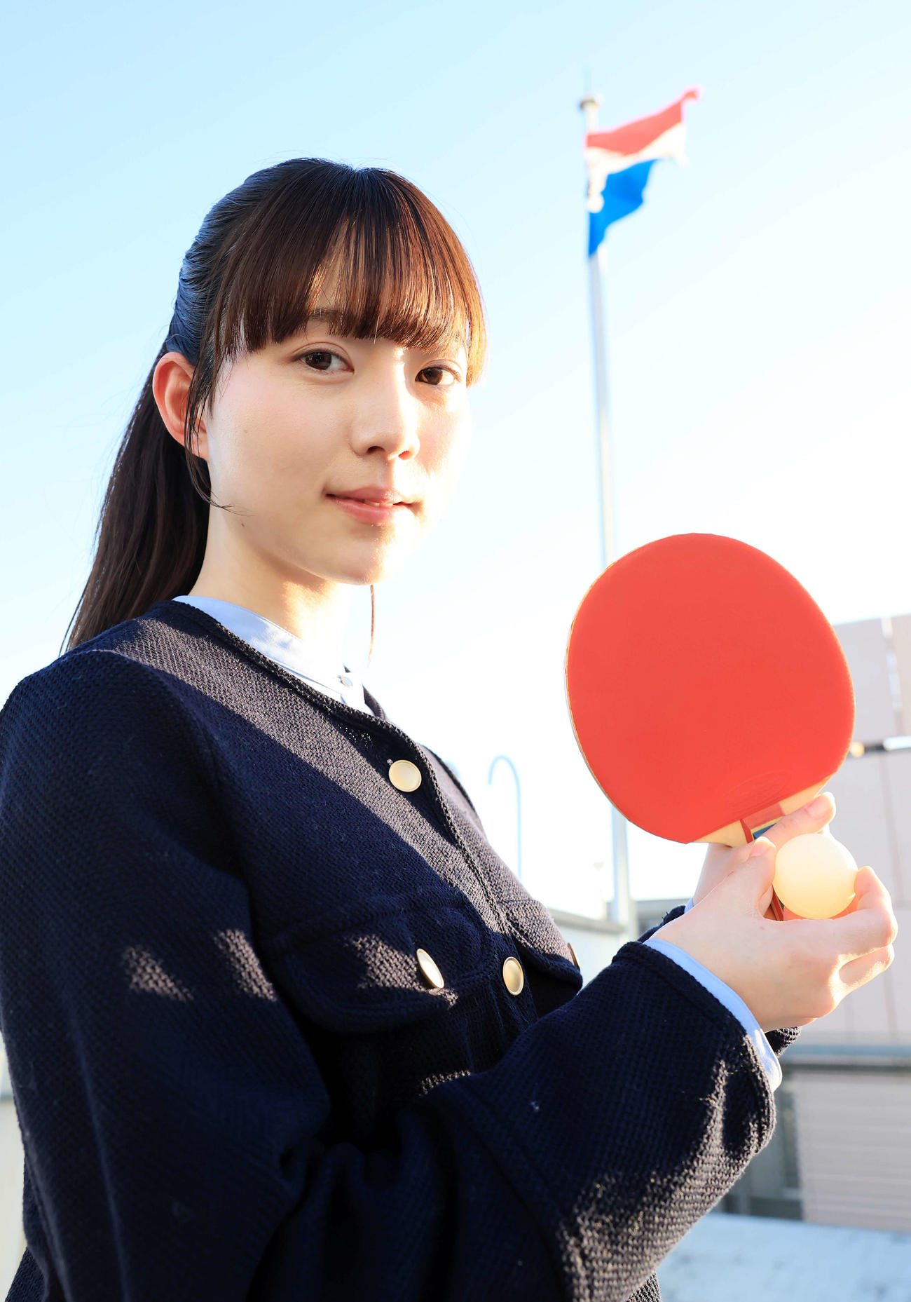 2025年2月25日、来社した“卓球天使”の菊池日菜は日刊スポーツの社旗を背にほほ笑む（撮影・浅見桂子）