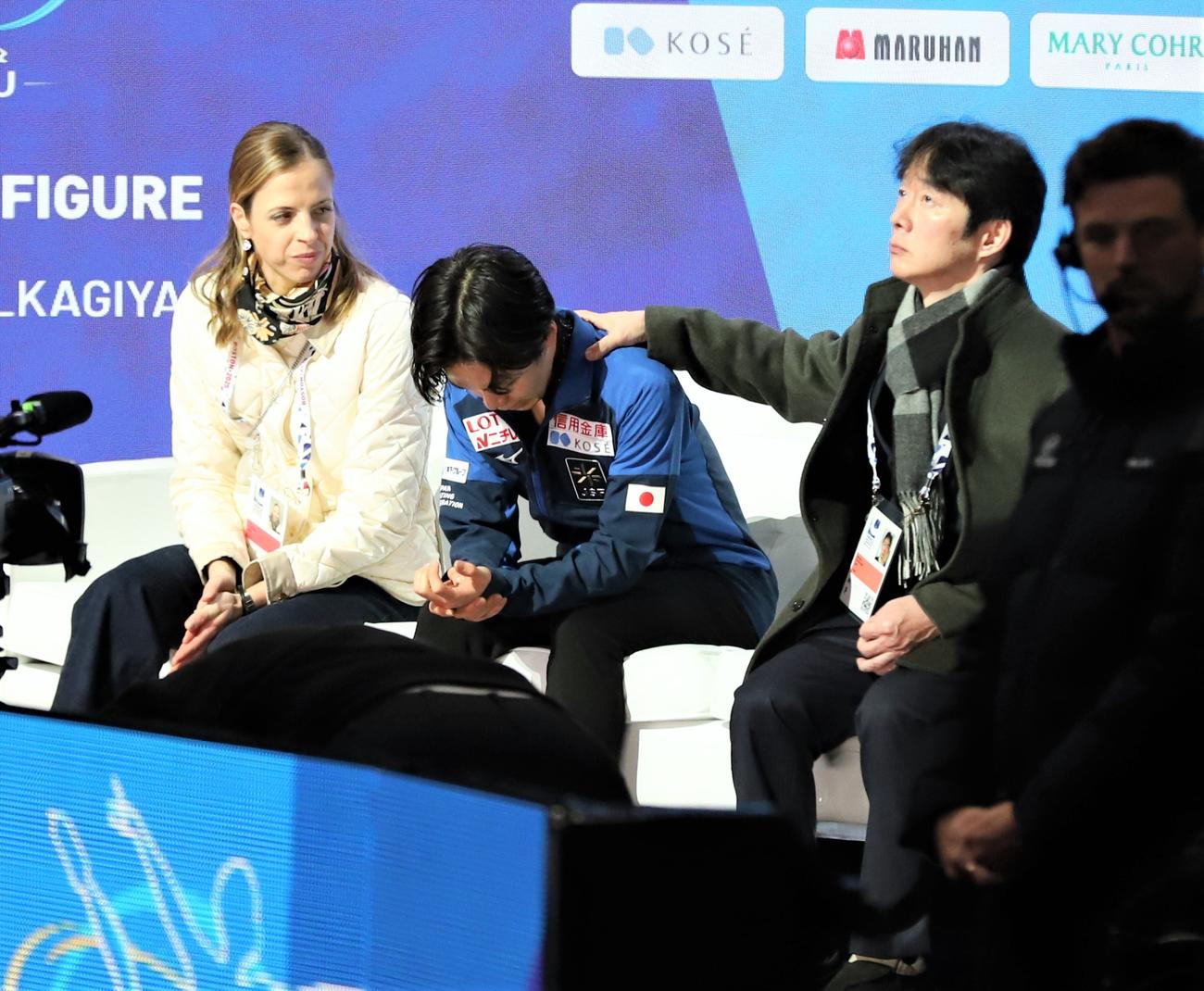 世界選手権男子フリー後のキス・アンド・クライでうつむく鍵山優真（中央）。左はカロリーナ・コストナー・コーチ、右は鍵山正和コーチ（撮影・藤塚大輔）