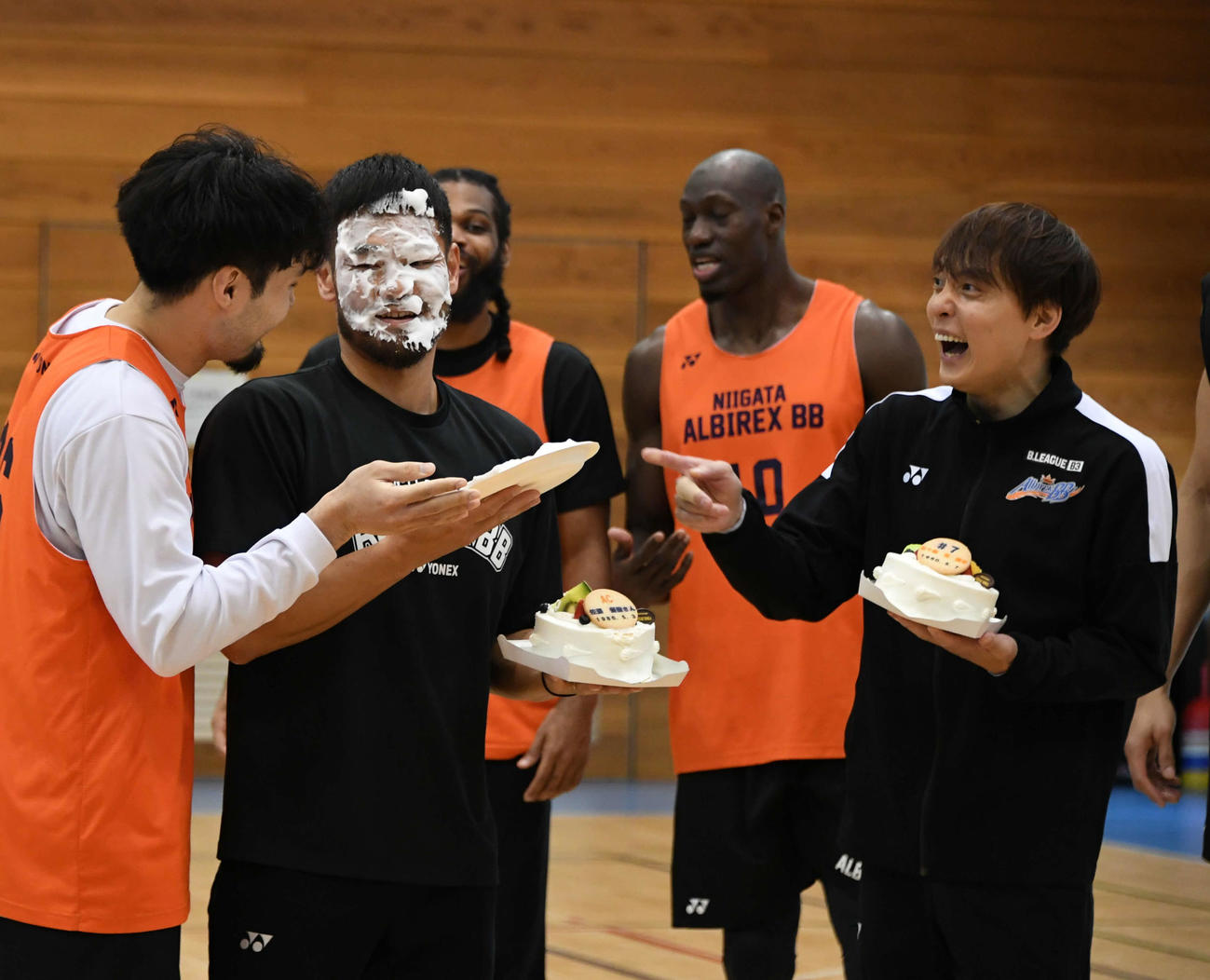 45歳の誕生祝いでケーキをプレゼントされた五十嵐（右）。同じく誕生祝いを受けた佐藤コーチ（左から2人目）がポーグ（左）からシェービングクリームの「ケーキ」を顔面に塗られたのを見て、驚きの表情