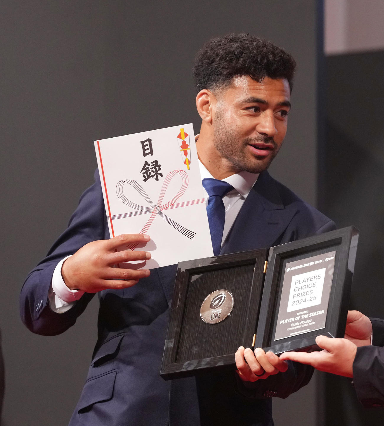 選手投票のプレーヤー・オブ・ザシーズンを受賞し、盾と副賞の肉の目録を手に笑顔を見せるBL東京モウンガ（撮影・足立雅史）