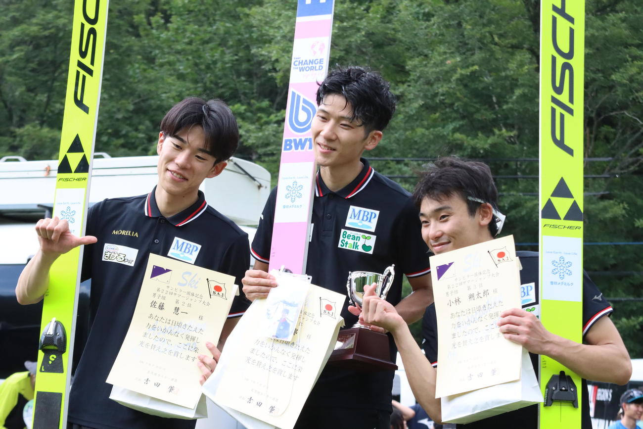 男子で表彰台を独占した雪印メグミルクのメンバー。左から2位の佐藤慧、坂野さんの写真を手に持つ優勝した佐藤幸、3位の小林朔（撮影・保坂果那）