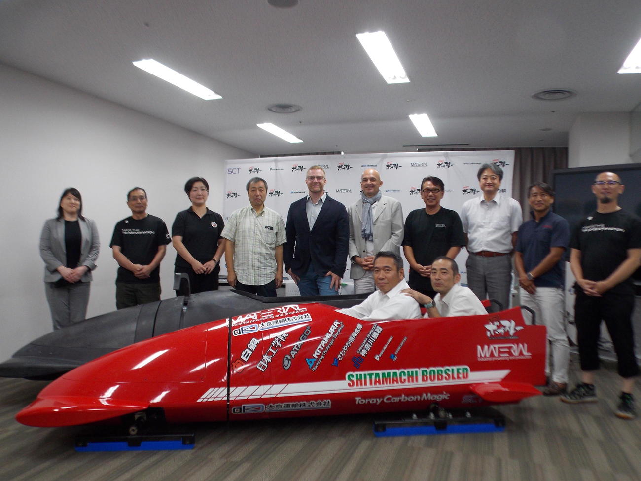 下町ボブスレーに乗った黒坂浩太郎委員長（前列左）とイタリアのマニュエル・マカタ監督（後列右から6人目）ら関係者（撮影・松本航）