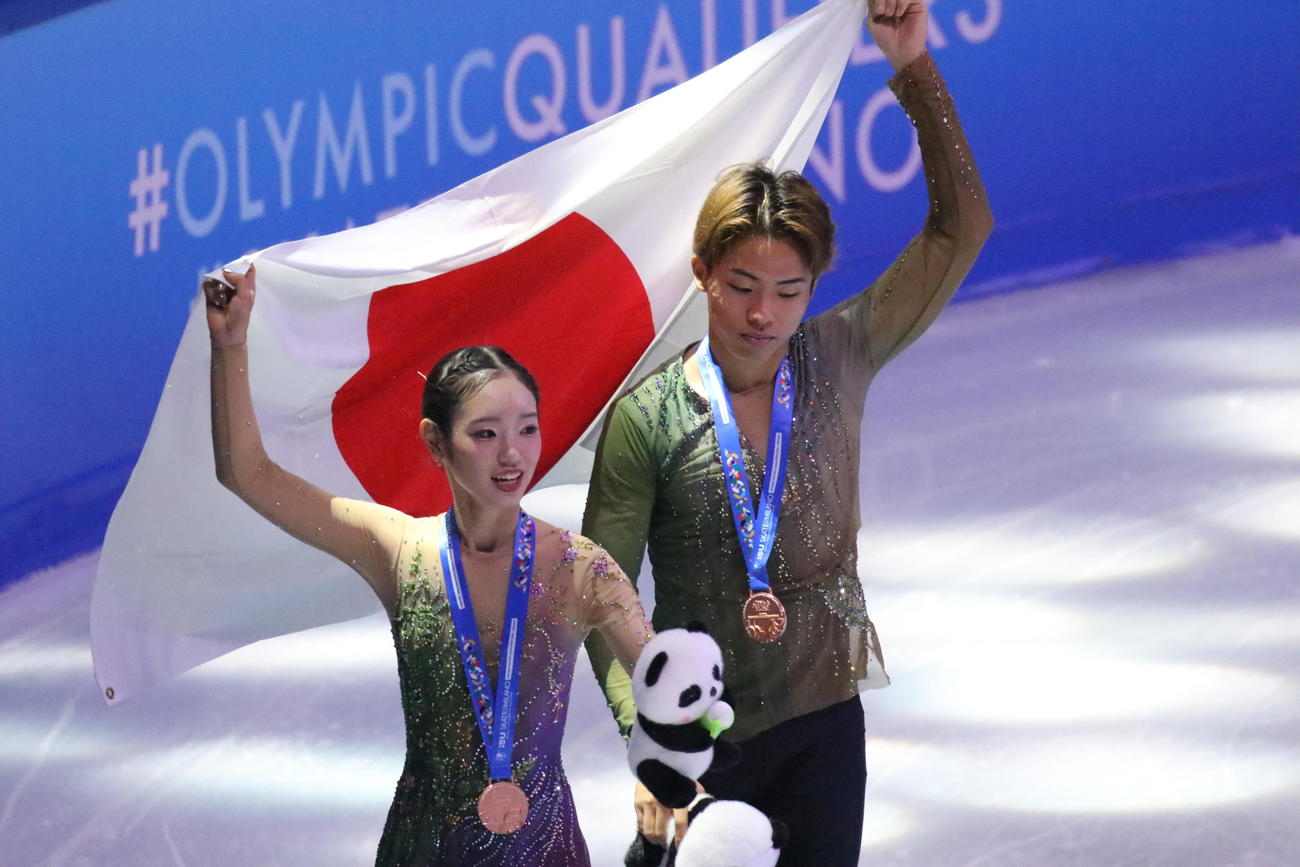 ミラノ・コルティナ冬季五輪最終予選ペアの表彰式で日の丸を手に笑顔を見せる長岡柚奈（左）と森口澄士（撮影・松本航）