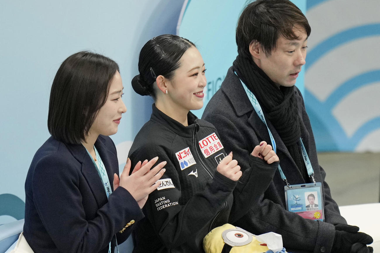 女子SPの得点を確認し、笑顔の青木祐奈（中央）。奥は中庭健介コーチ＝北京（共同）