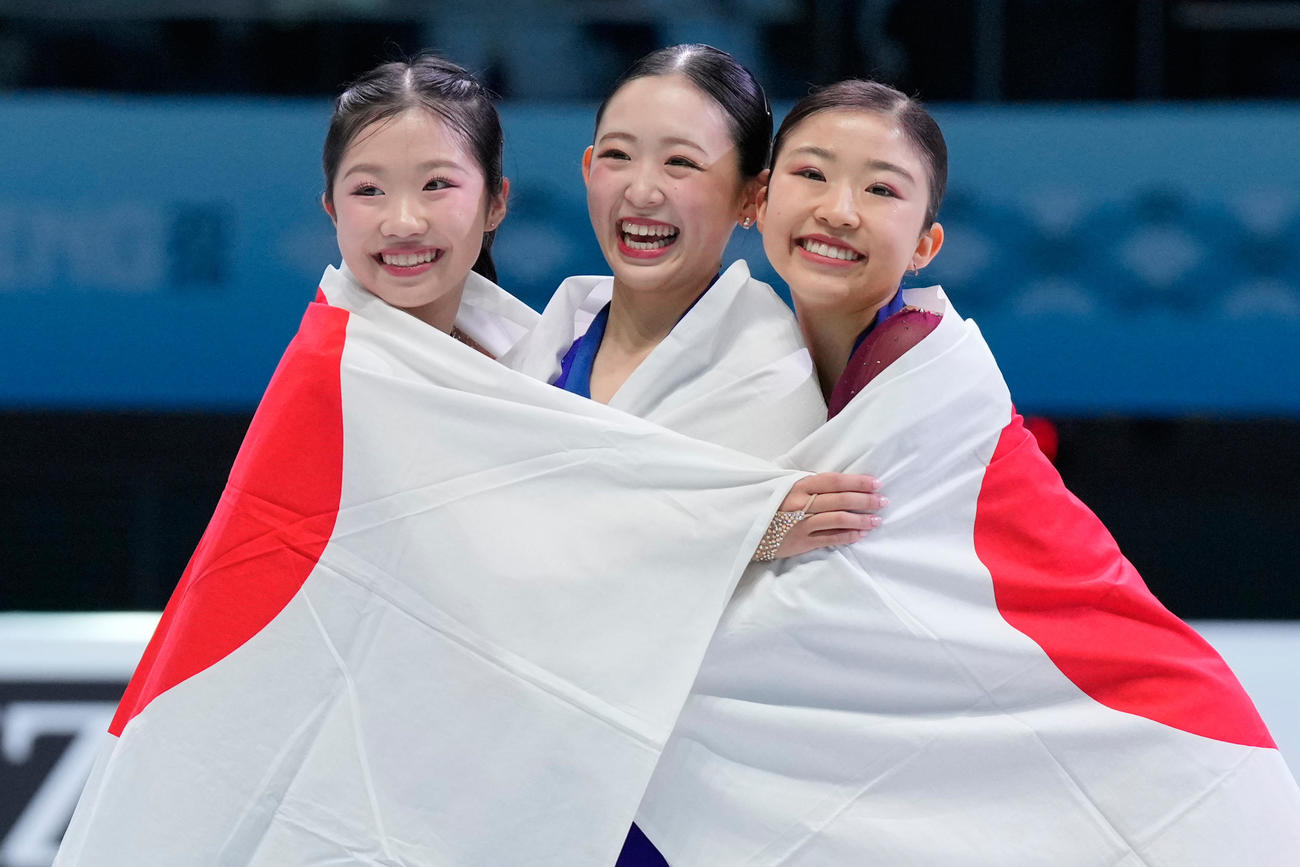 表彰台で日の丸にくるまって笑顔を見せる、左から2位の中井亜美、1位の青木祐奈、3位の千葉百音（AP）