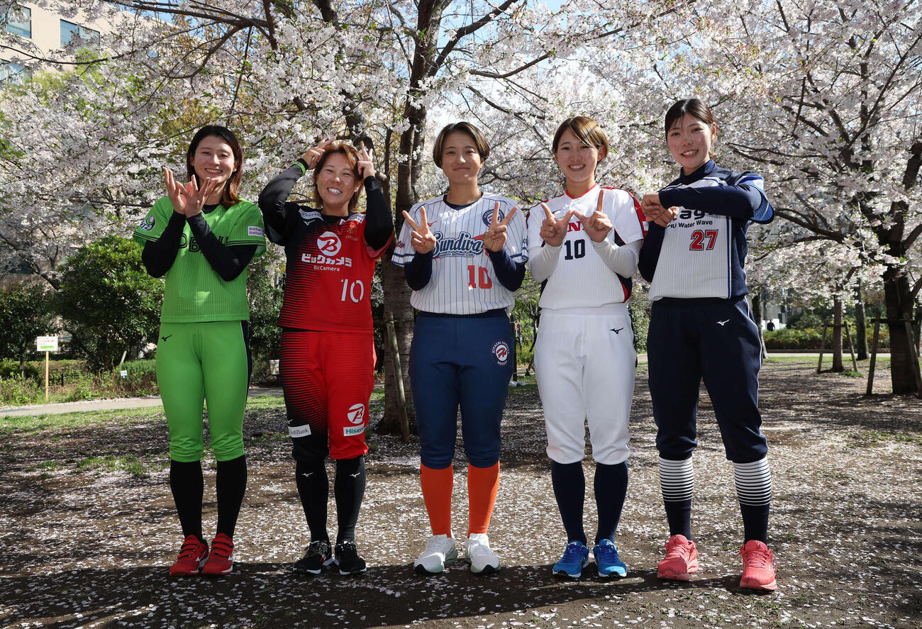 桜の下でポーズを決めるソフトボール女子JDリーグの、左から伊予銀行の辻井美波さん、ビックカメラ高崎の内藤実穂さん、日立の笠原朱里さん、ホンダの大川茉由さん、タカギ北九州の鹿野愛音さん（撮影・丹羽敏通）