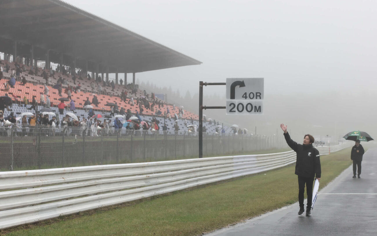スーパーフォーミュラ第3戦　強い雨脚と霧が立ちこめる中で中止が決定し、コースに出てファンに手を振って歩く近藤真彦会長（JRP提供）＝2026年4月26日、大分県日田市のオートポリス