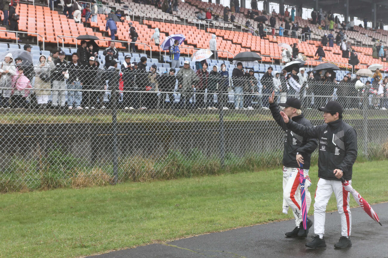 スーパーフォーミュラ第3戦　強い雨脚と霧が立ちこめる中で中止が決定し、コースに出てファンに手を振って歩く牧野任祐（左）と太田格之進（JRP提供）＝2026年4月26日、大分県日田市のオートポリス