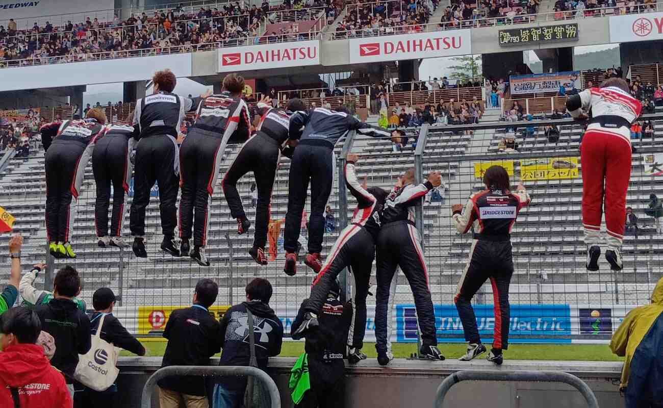 クラス優勝を決めたマシンへ金網から身を乗り出して手を振る同僚ドライバー