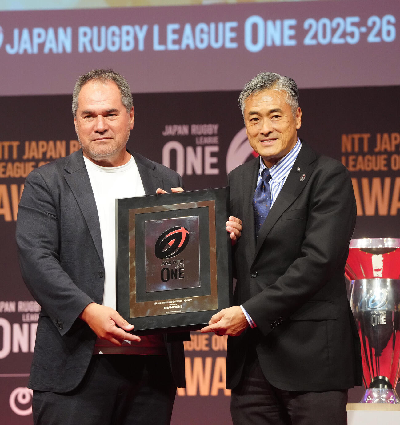 ラグビー・リーグワンの表彰式で表彰されるD1優勝の神戸デイブ・レニー・ヘッドコーチ（左）。右は玉塚元一理事長（撮影・江口和貴）＝2026年6月8日