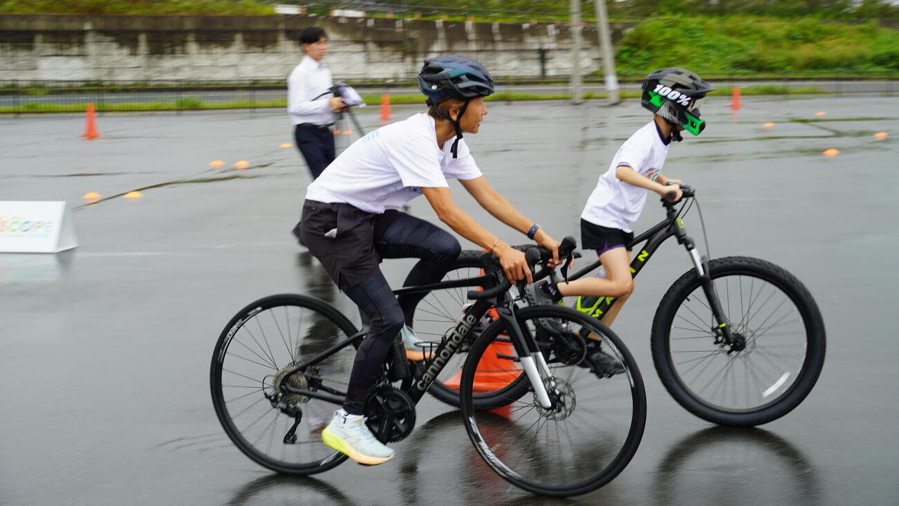 参加者に並走してバイク指導をする関根明子氏（左）
