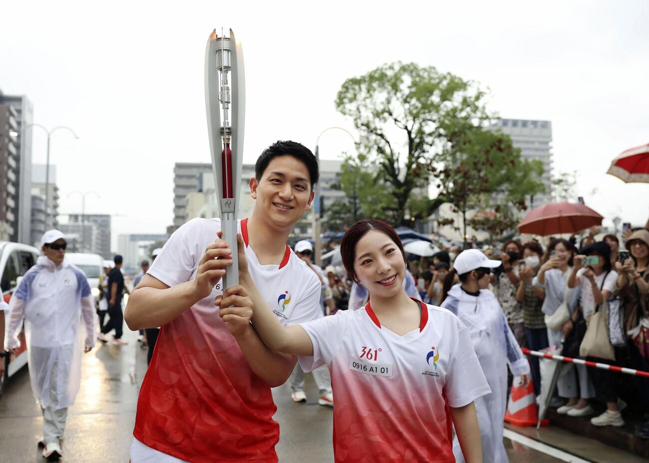 愛知・名古屋アジア大会の聖火リレーでランナーを務め、2人でトーチを掲げるミラノ・コルティナ冬季五輪金メダルの三浦璃来さん（右）と木原龍一さん＝16日午後、名古屋市瑞穂区（代表撮影）