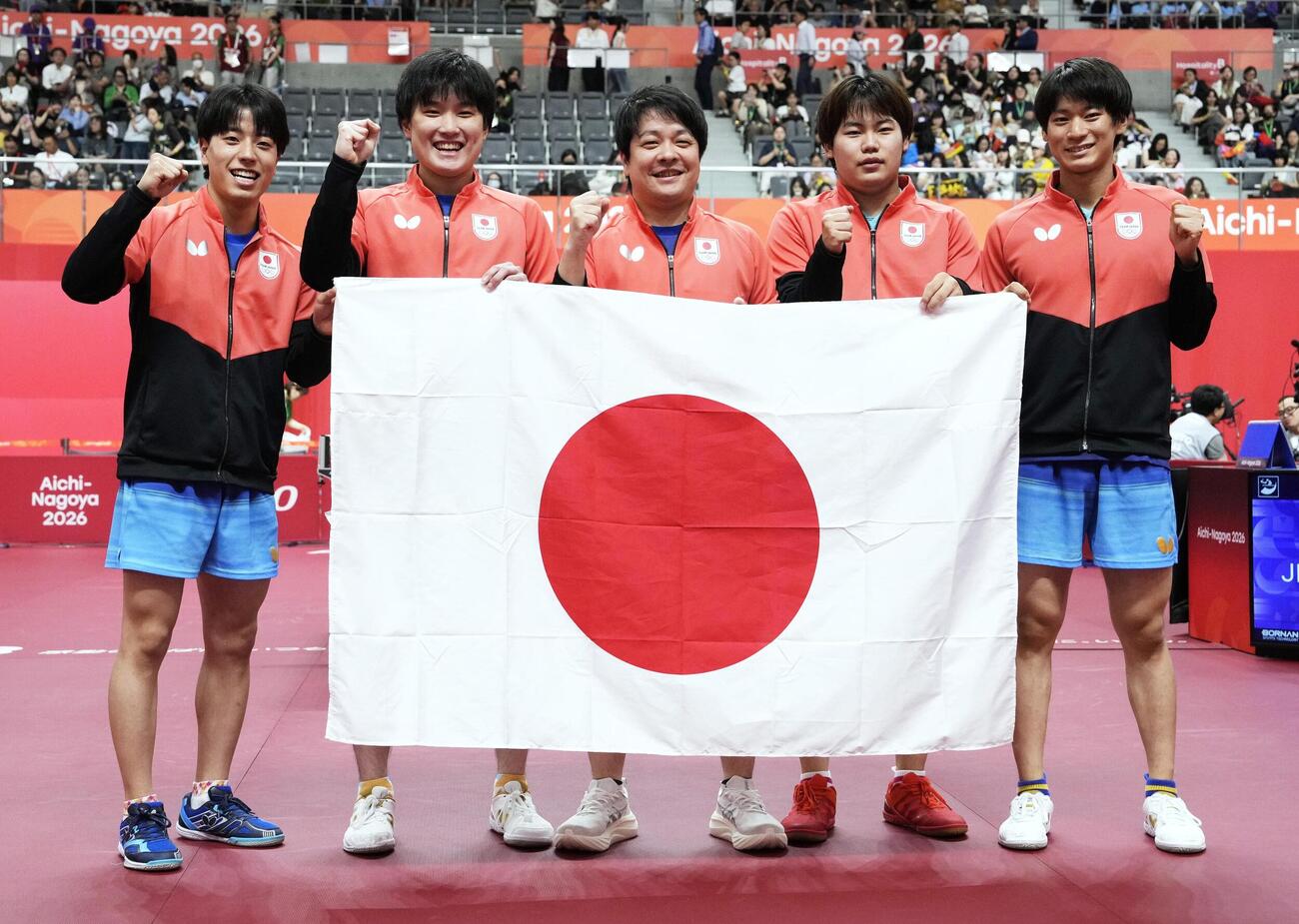 男子団体で優勝し、日の丸を掲げる（左から）篠塚大登、張本智和、岸川聖也監督、松島輝空、戸上隼輔＝豊田市総合体育館