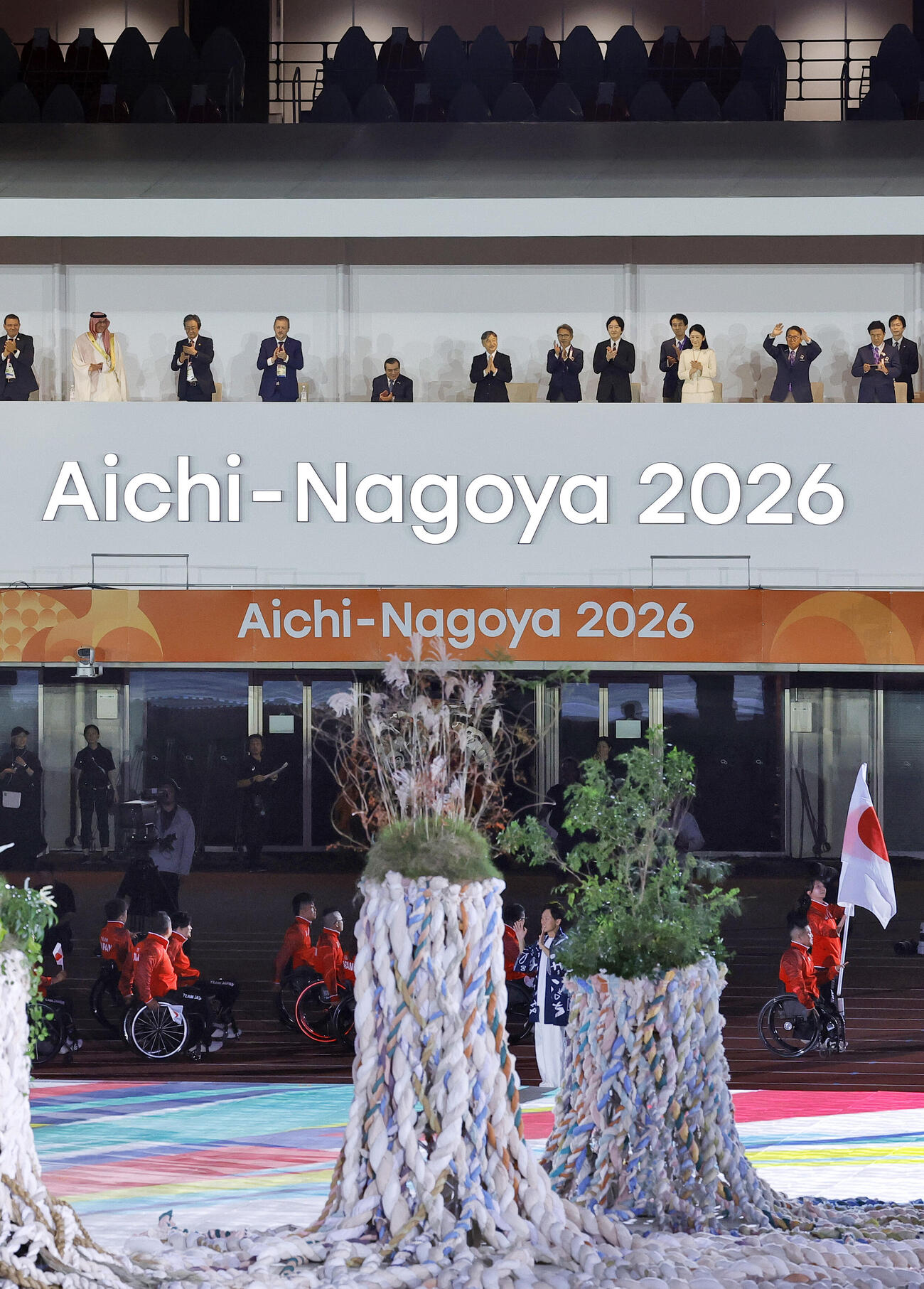 開会式で入場行進する日本選手団（下）に拍手を送られる天皇陛下と秋篠宮ご夫妻＝18日、パロマ瑞穂スタジアム（共同）