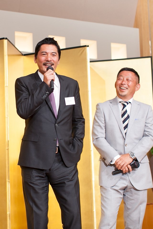 14年5月に開かれた伏見工山口総監督の祝賀会で壇上に立った高崎氏（右）と平尾さん（高崎氏提供）