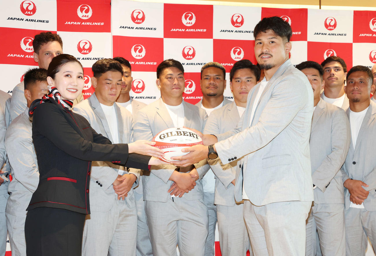 ラグビー日本代表出発式でラグビーボールをJAL職員に渡す姫野主将（手前右）（撮影・宮地輝）