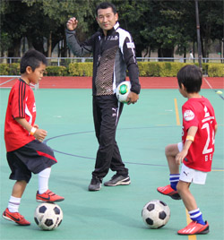 少年のドリブルを見守る都並氏